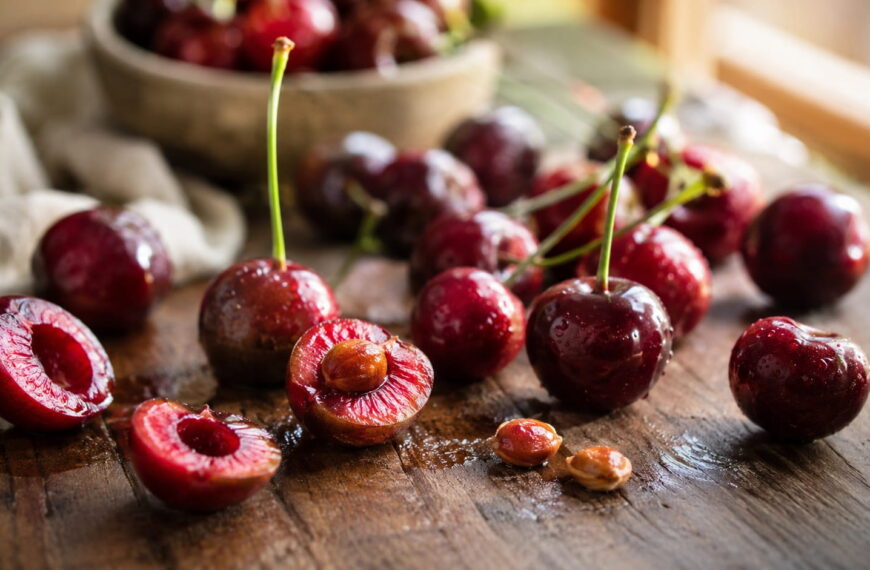 Fresh ripe cherries with several cherry pits on a rustic wooden table illustrating symptoms of cyanide poisoning from cherry pits and safe cherry pit handling.