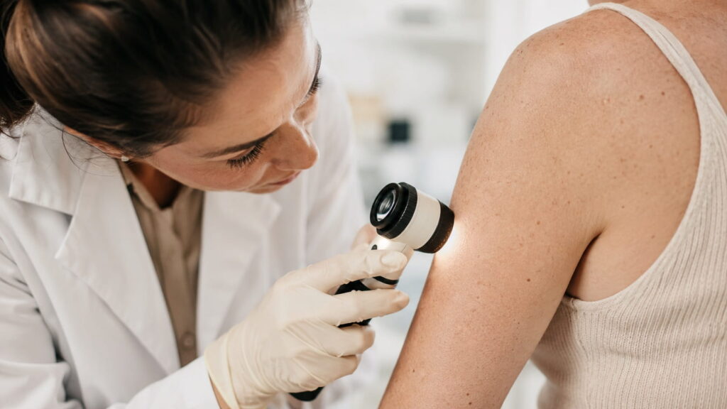 Dermatologist using a dermatoscope to examine a patient's skin on the shoulder during a skin health consultation